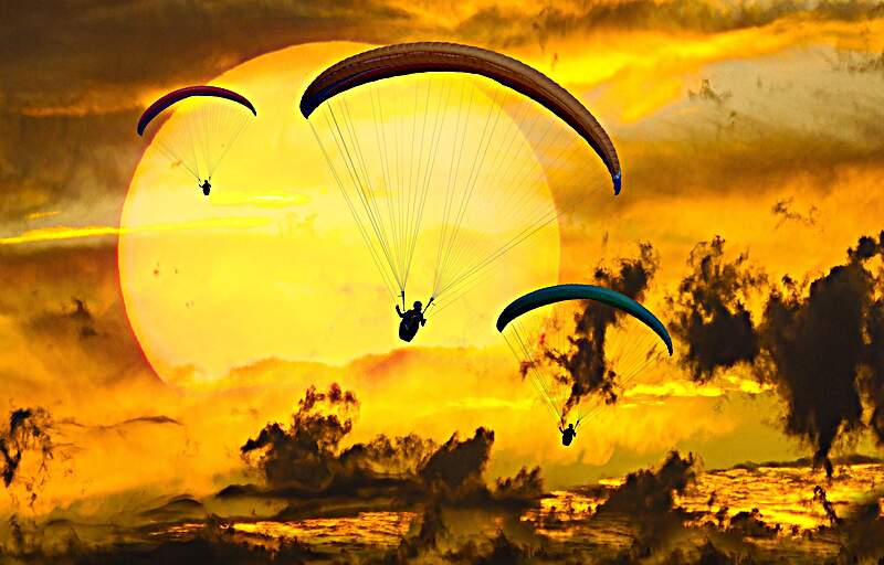 Three paragliders set against sunset